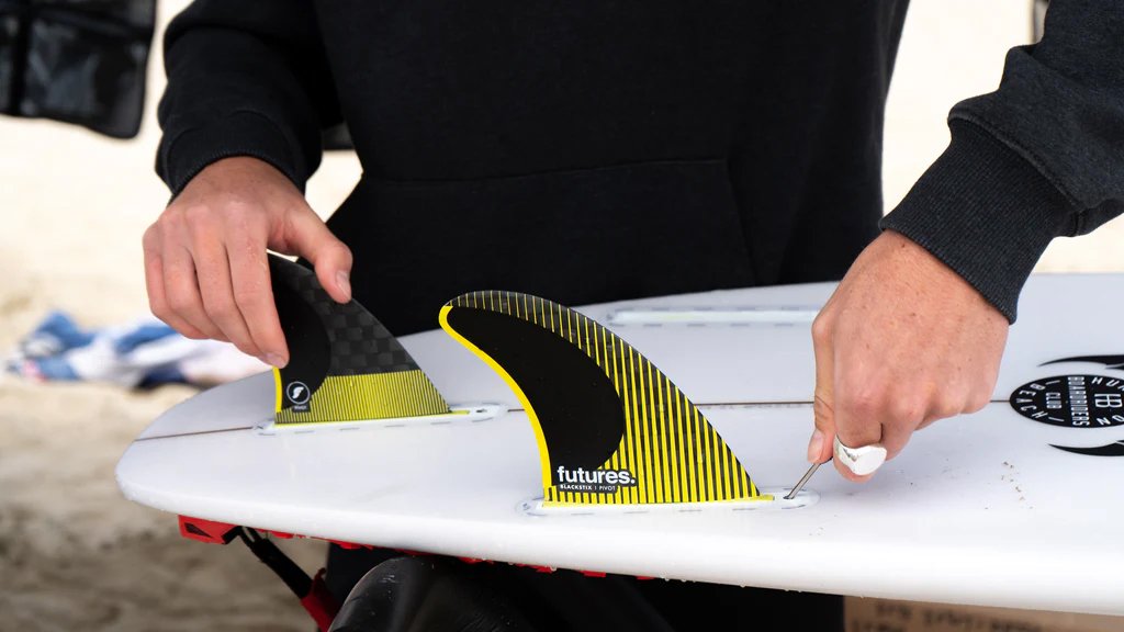Surfista instalando quilhas Futures em prancha de surf, comparável ao sistema FCS